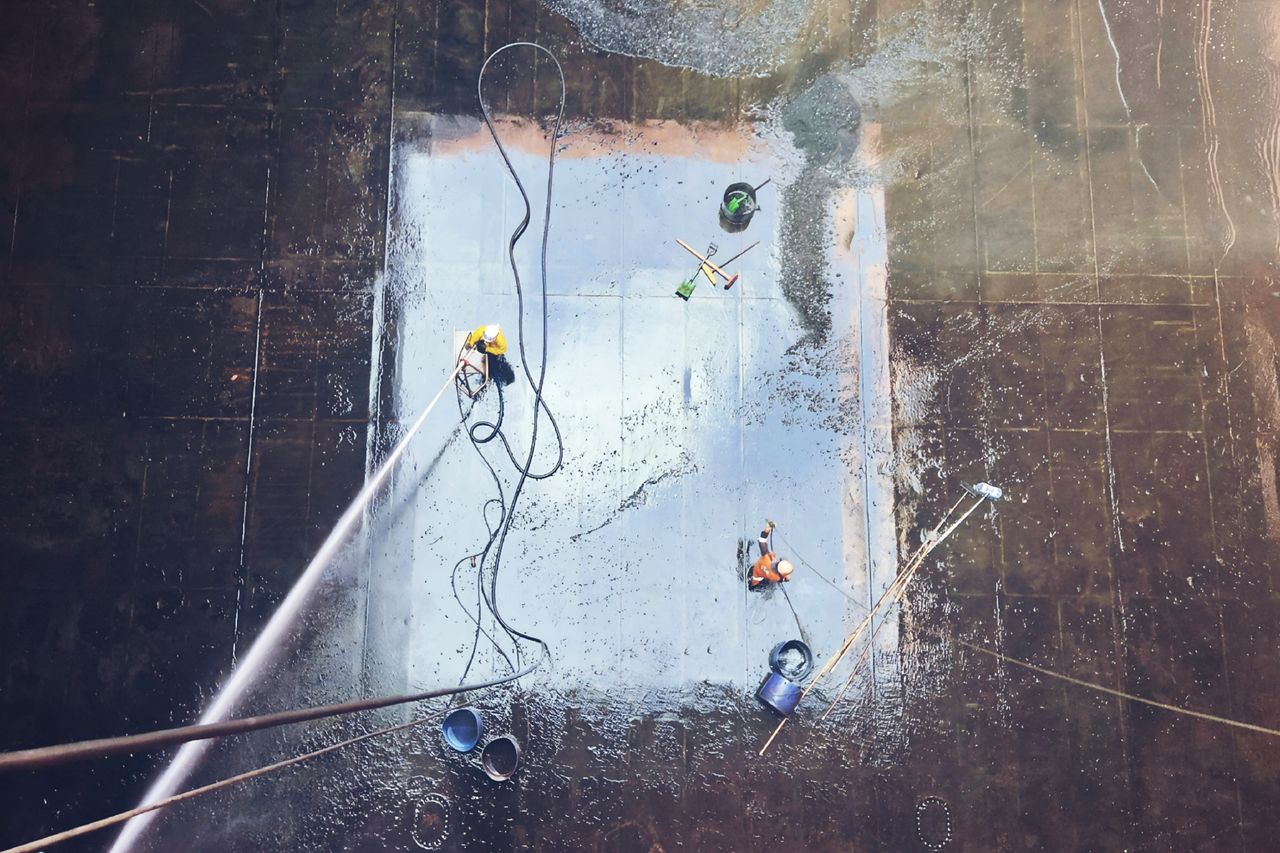 services-01 Top view of workers cleaning a large surface with equipment and water hoses.